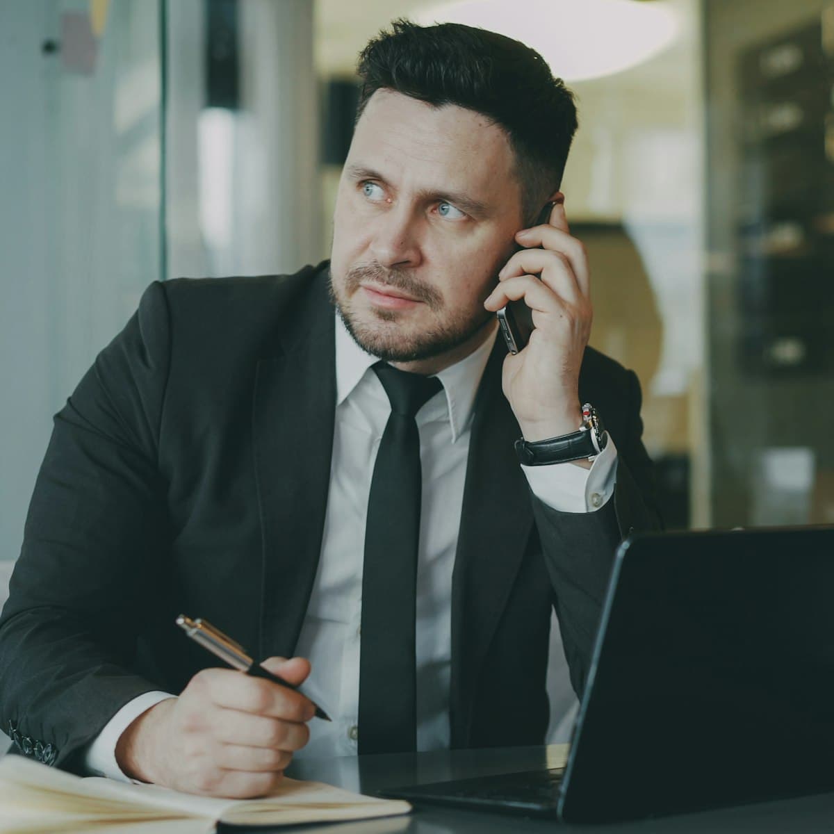 A loan officer on a call at their desk, taking notes beside a laptop