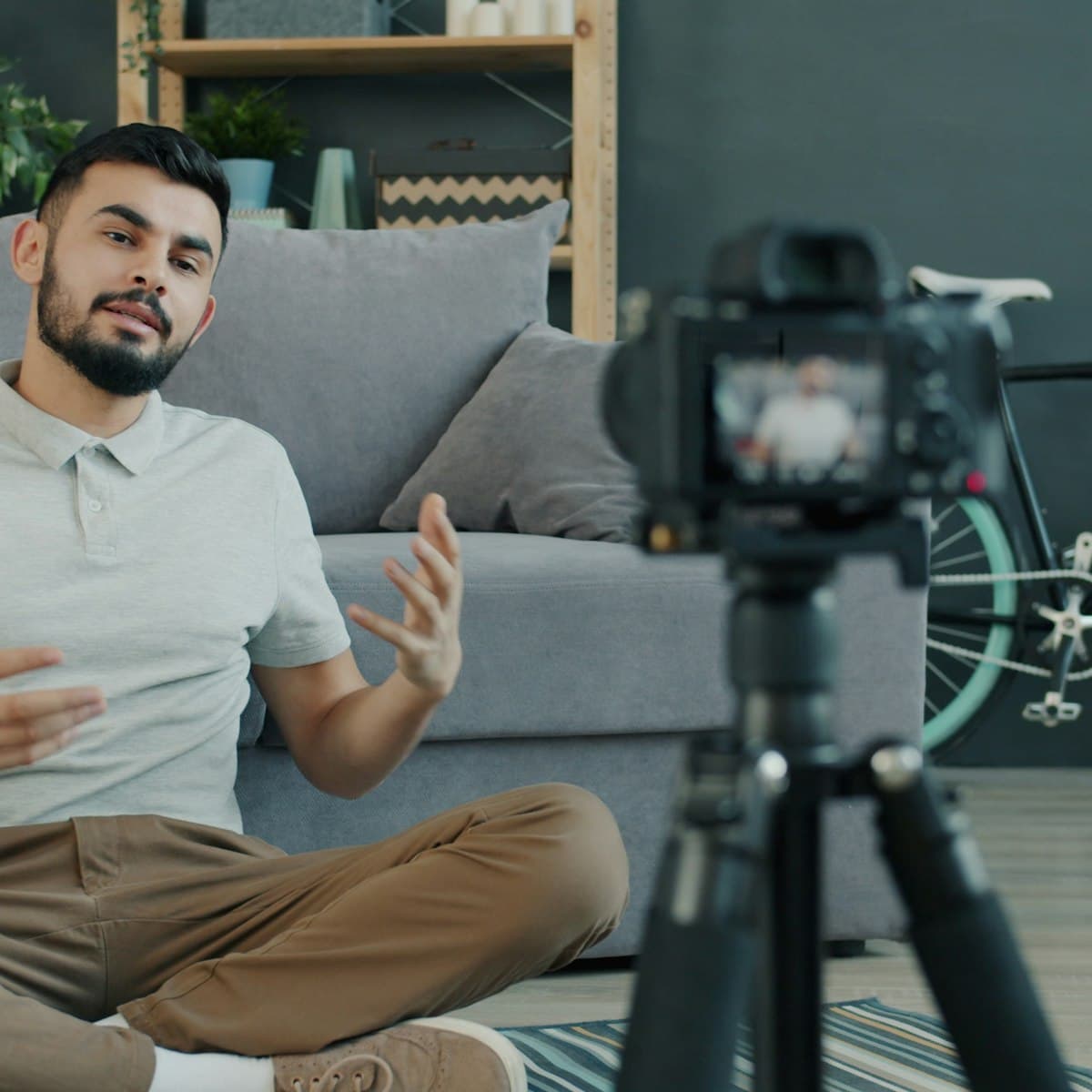 A man talking to a camera on a tripod, recording a video at home